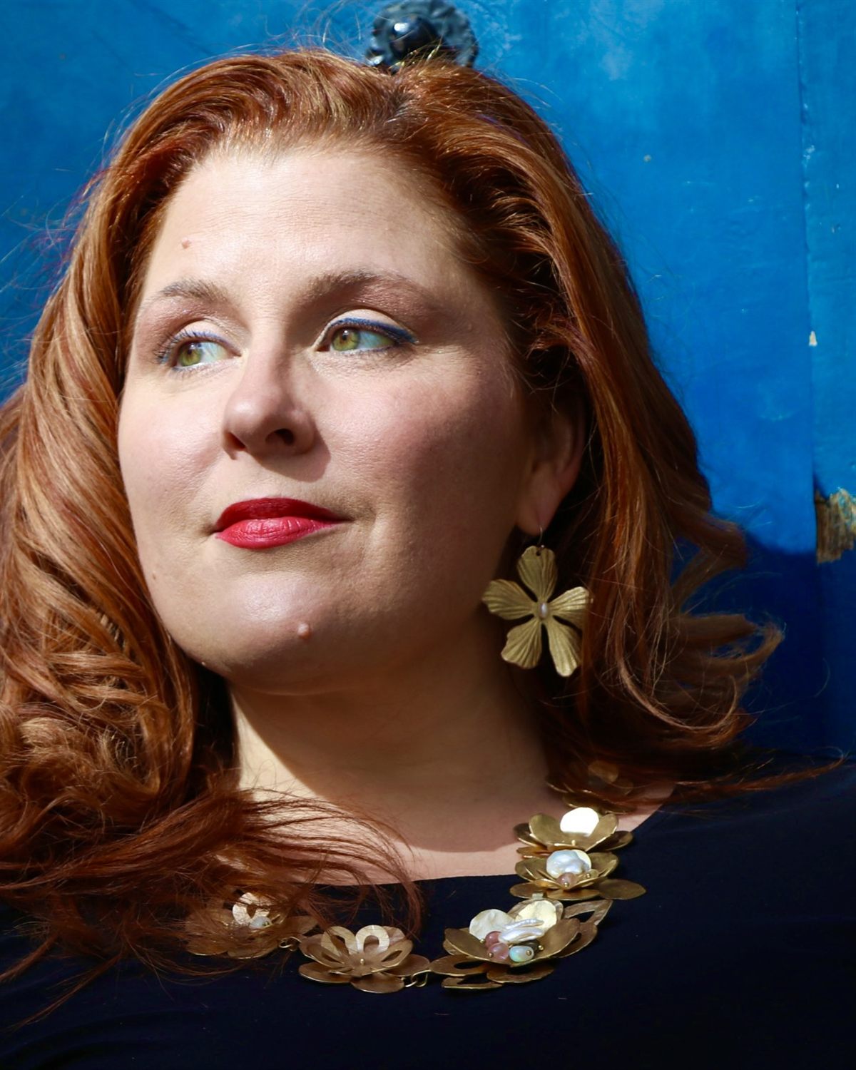 Jenn Quader in profile against the cobalt Paris door, chin lifted, gold flower earring catching the light.