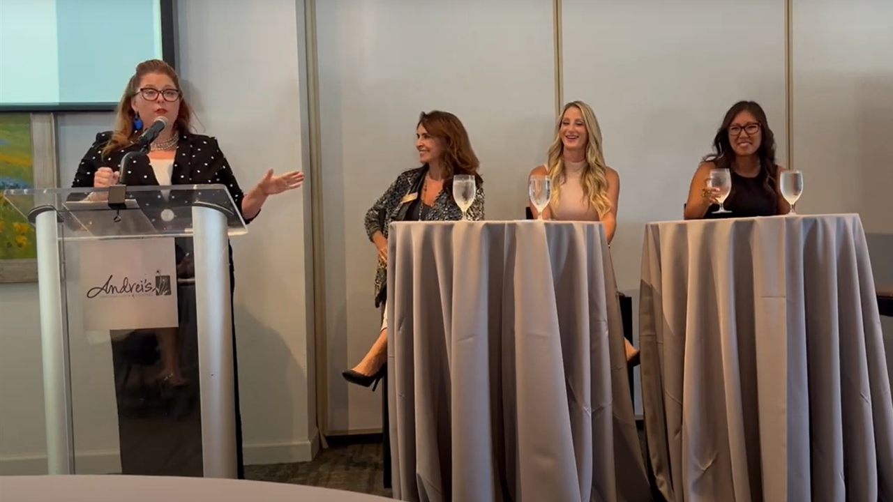 Jenn Quader at a lectern moderating a CREW Orange County panel, three panellists at high tables beside her.