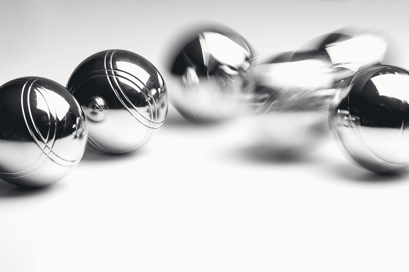 Four polished steel bocce balls on a pale surface, one of them blurred in mid-roll.