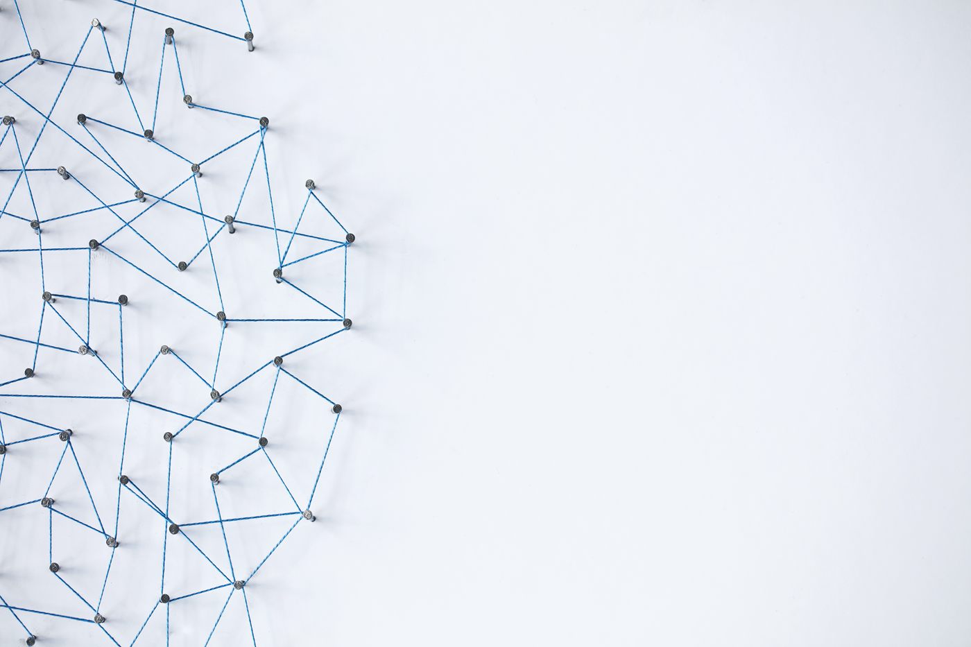 Dozens of pins on a white board joined to one another by blue thread into a dense web.