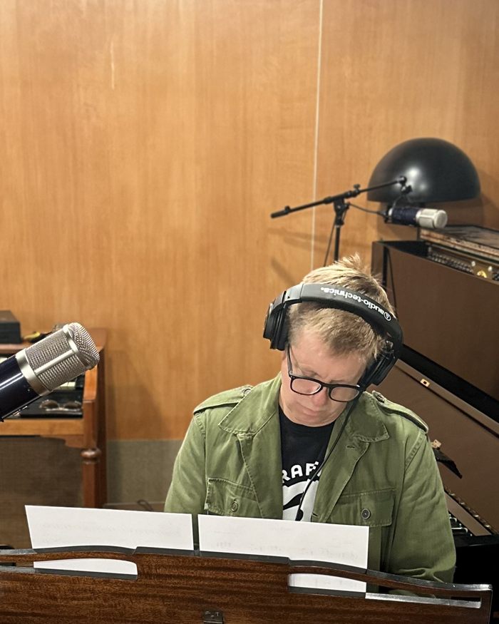 Jeff Babko at the piano in headphones, reading a chart, seen from across the open lid of a grand piano.