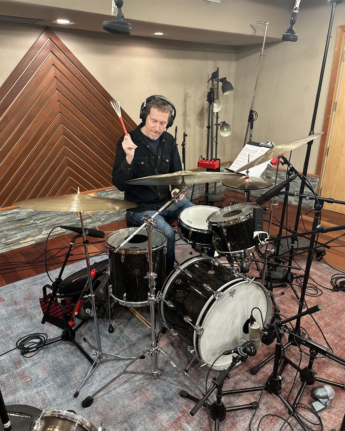 Zach Danziger behind a drum kit in headphones, brushes raised, ride and crash cymbals close-miked around him.